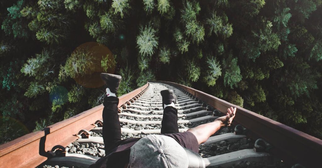 A man poses daringly over train tracks with a forest view.